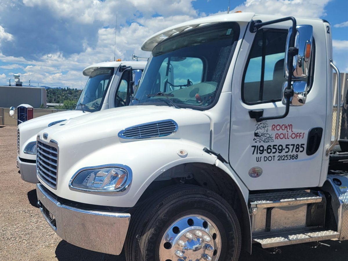 Two white Rock'n Roll-Offs trucks parked side by side in Colorado Springs